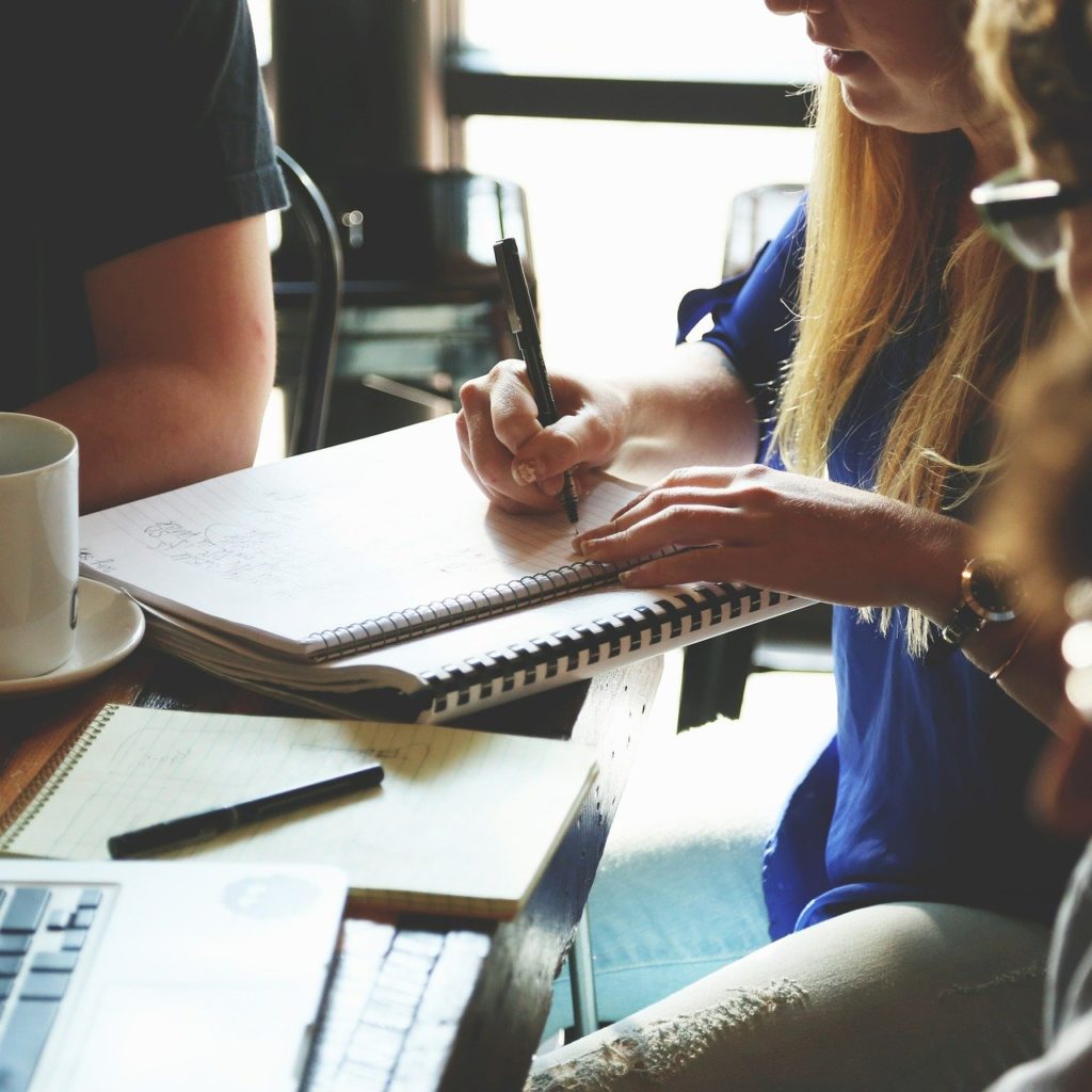 Mulher representando a liderança do grupo, anotando em um caderno e outras duas pessoas a seu lado